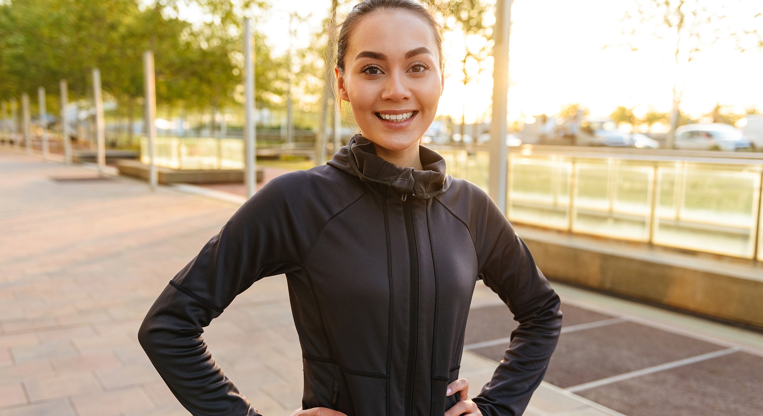 Smiling woman in athletic wear outdoors at sunset.