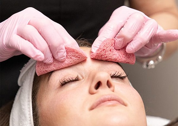 Facial treatment with sponges on client's forehead.